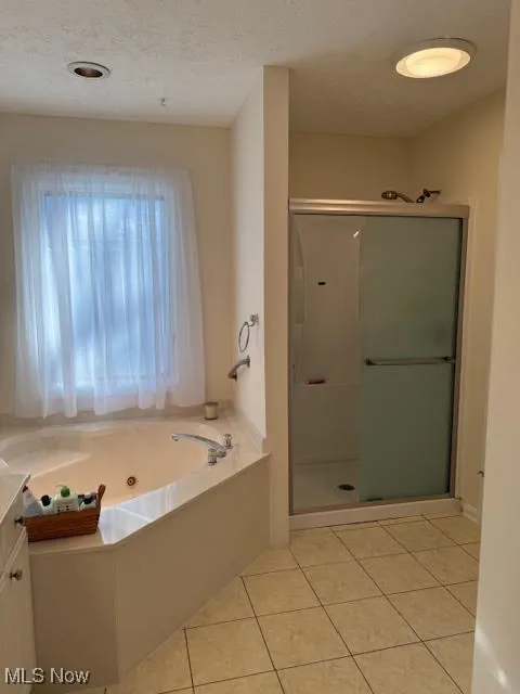 Bathroom with a tub with jets, a shower stall, light tile patterned floors, a textured ceiling, and vanity