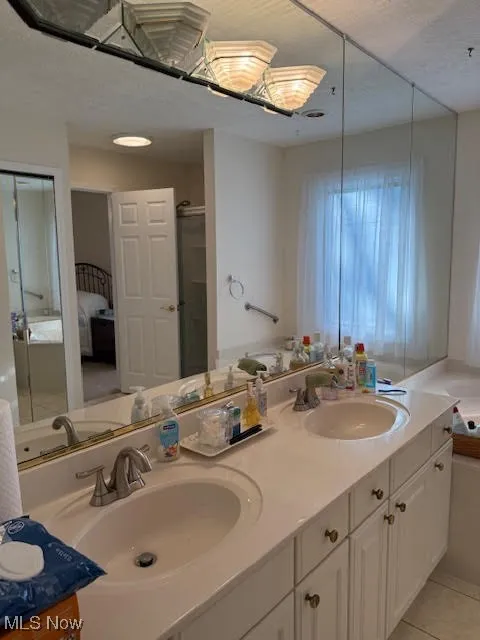 Full bathroom featuring connected bathroom, double vanity, a stall shower, light tile patterned floors, and a textured ceiling