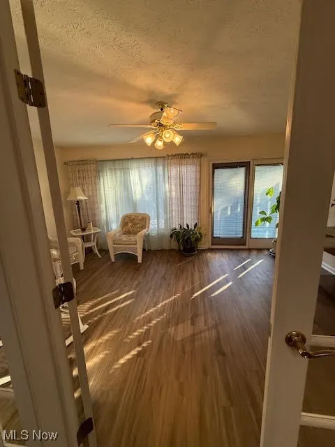 Sitting room featuring a textured ceiling, dark wood-style floors, and ceiling fan