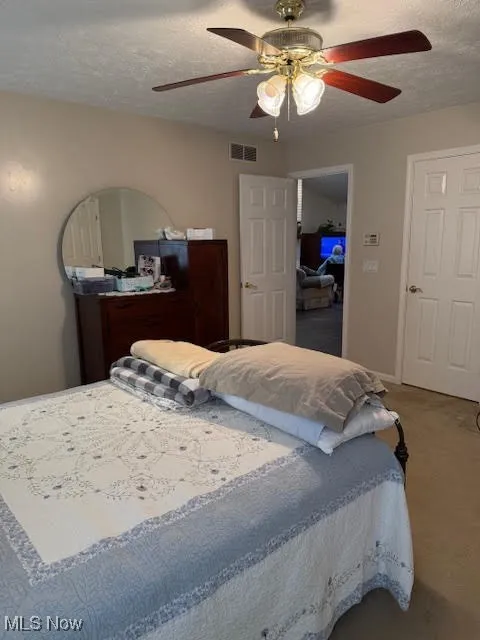 Bedroom with a textured ceiling, a ceiling fan, and carpet flooring