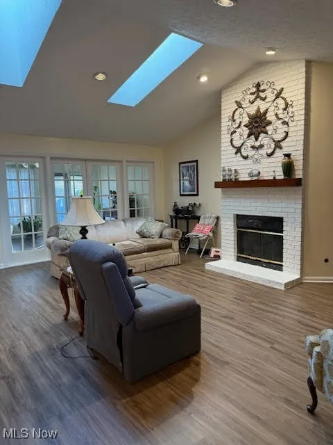 Living room featuring vaulted ceiling, a brick fireplace, wood finished floors, recessed lighting, and a skylight