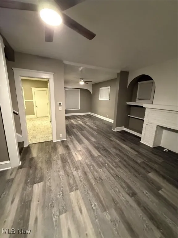 Unfurnished living room featuring dark wood-type flooring and a ceiling fan