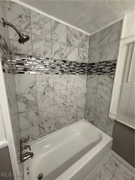 Bathroom with marble look tiles, shower / bathtub combination, and a textured ceiling