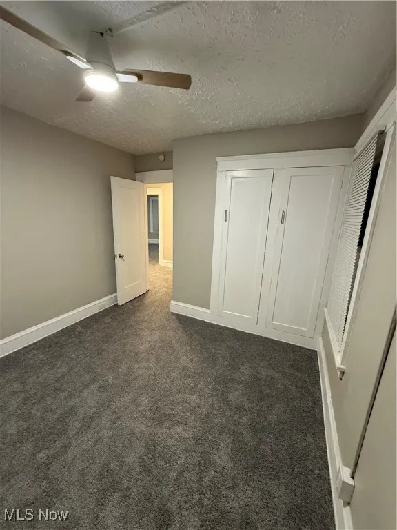 Unfurnished bedroom with dark colored carpet, ceiling fan, and a textured ceiling
