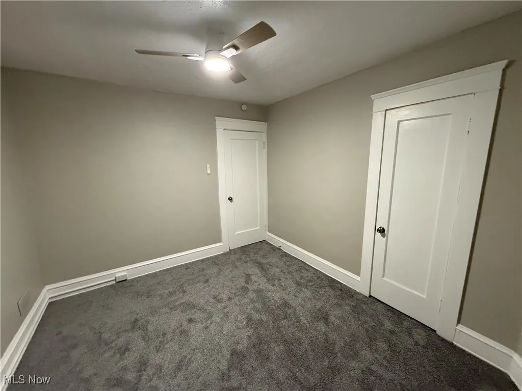 Empty room featuring dark colored carpet and ceiling fan