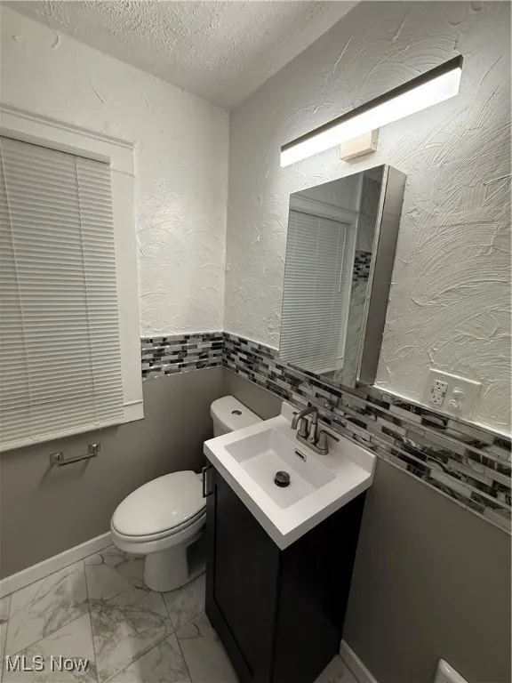 Half bath with a textured ceiling, light marble finish flooring, vanity, a textured wall, and backsplash