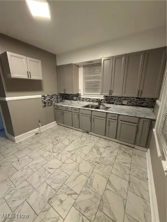 Kitchen with gray cabinets, light marble finish flooring, and decorative backsplash