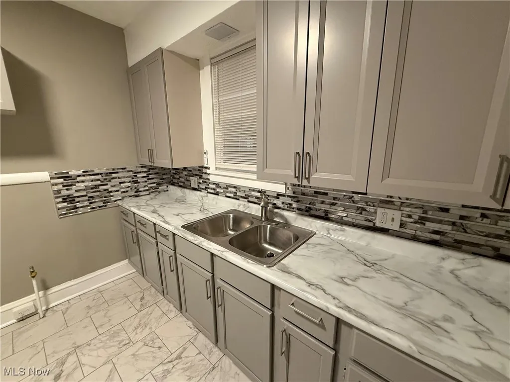 Kitchen featuring backsplash, gray cabinets, light marble finish flooring, and light stone countertops