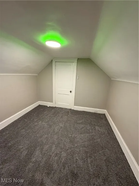 Additional living space with lofted ceiling and dark colored carpet
