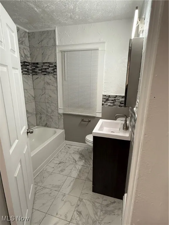 Bathroom with light marble finish floors, vanity, shower / washtub combination, a textured wall, and a textured ceiling