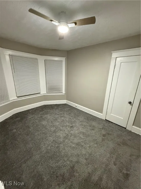 Unfurnished bedroom with a ceiling fan, a textured ceiling, and dark carpet