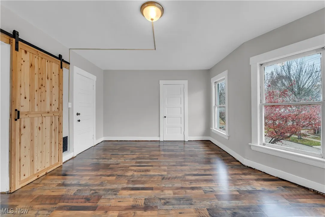 Unfurnished bedroom featuring a barn door and dark wood-type flooring