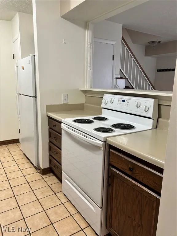 Kitchen with white range with electric cooktop, dark brown cabinets, refrigerator, light countertops, and a textured ceiling