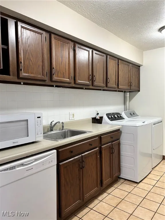 Washroom featuring a textured ceiling, washing machine and dryer, and light tile patterned floors