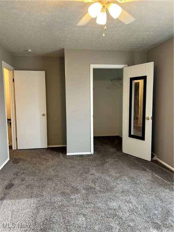 Unfurnished bedroom featuring carpet floors, a closet, a textured ceiling, and ceiling fan