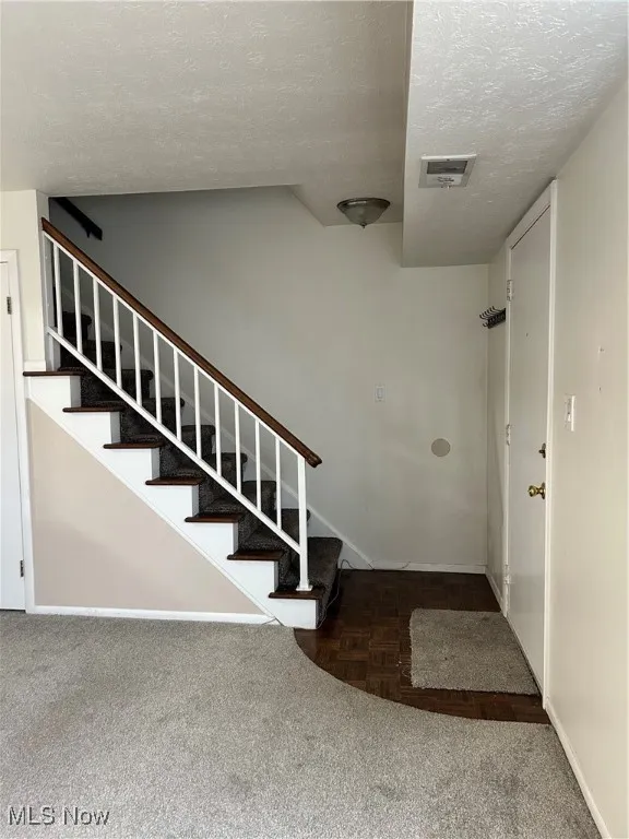 Staircase featuring a textured ceiling and carpet