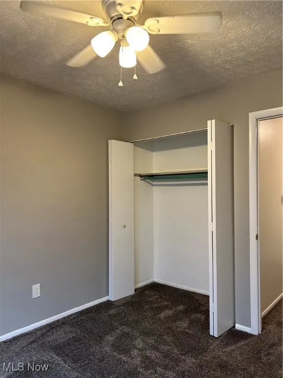 Unfurnished bedroom featuring a textured ceiling, dark colored carpet, ceiling fan, and a closet