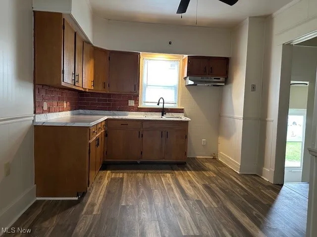 Kitchen with light countertops, dark wood-style floors, a ceiling fan, brown cabinets, and tasteful backsplash