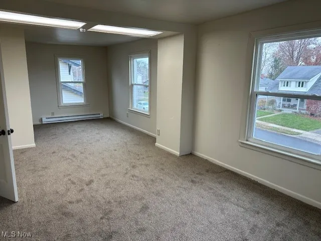 Carpeted spare room with plenty of natural light and a baseboard radiator