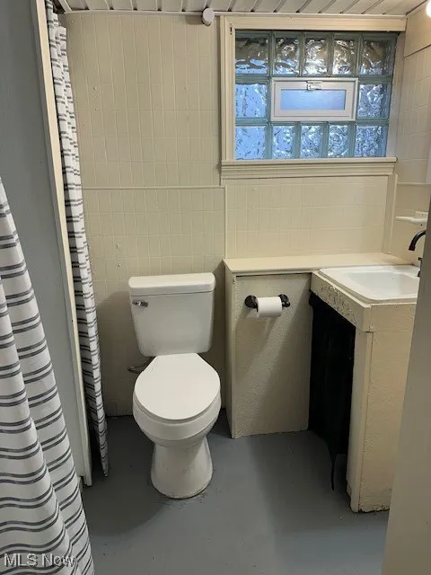 Full bath featuring tile walls, curtained shower, vanity, and finished concrete floors