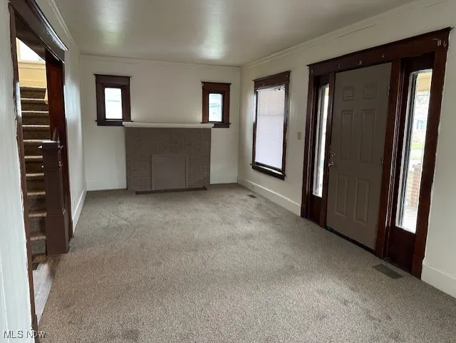 Foyer entrance with crown molding, carpet floors, stairs, and a fireplace
