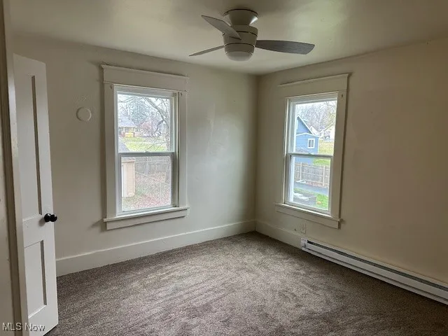 Unfurnished room featuring a baseboard heating unit, carpet, plenty of natural light, and a ceiling fan