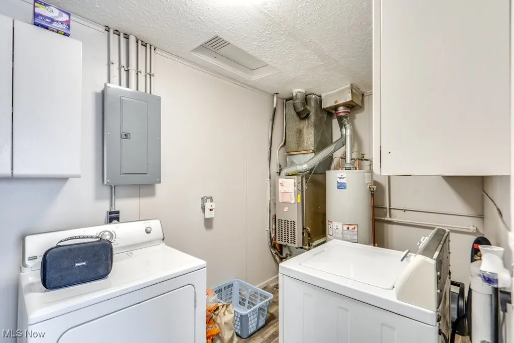 Laundry area with cabinet space, a textured ceiling, electric panel, washing machine and dryer, and gas water heater