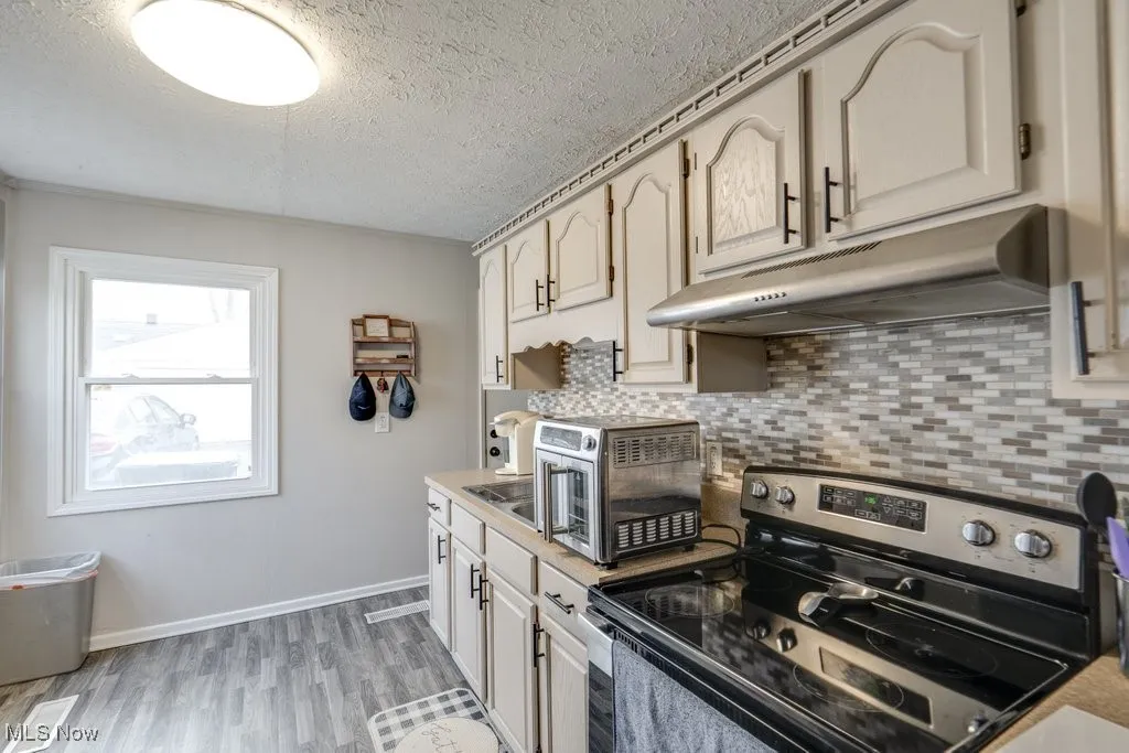 Kitchen with stainless steel electric range, light countertops, under cabinet range hood, a textured ceiling, and light wood finished floors