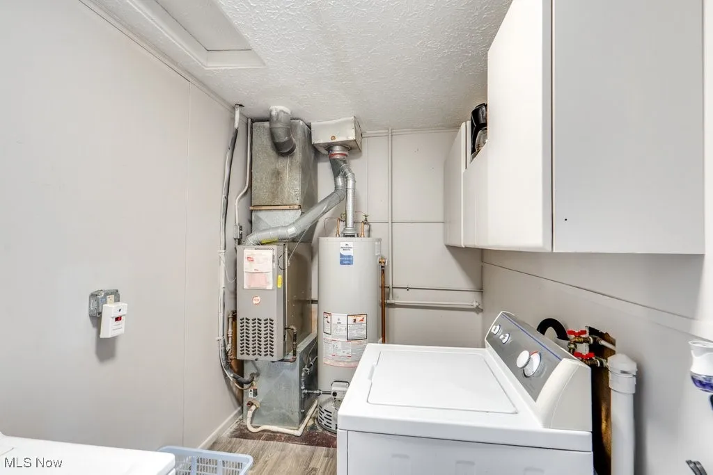 Washroom featuring a textured ceiling, gas water heater, cabinet space, heating unit, and wood finished floors