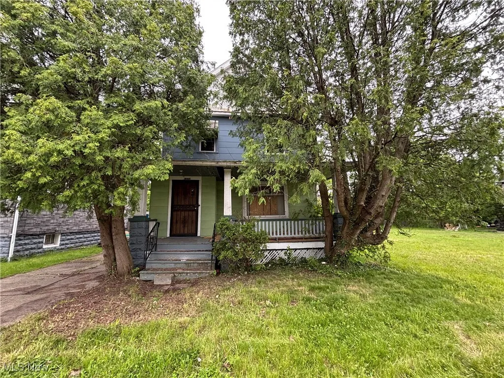 View of property hidden behind natural elements featuring covered porch and a front yard