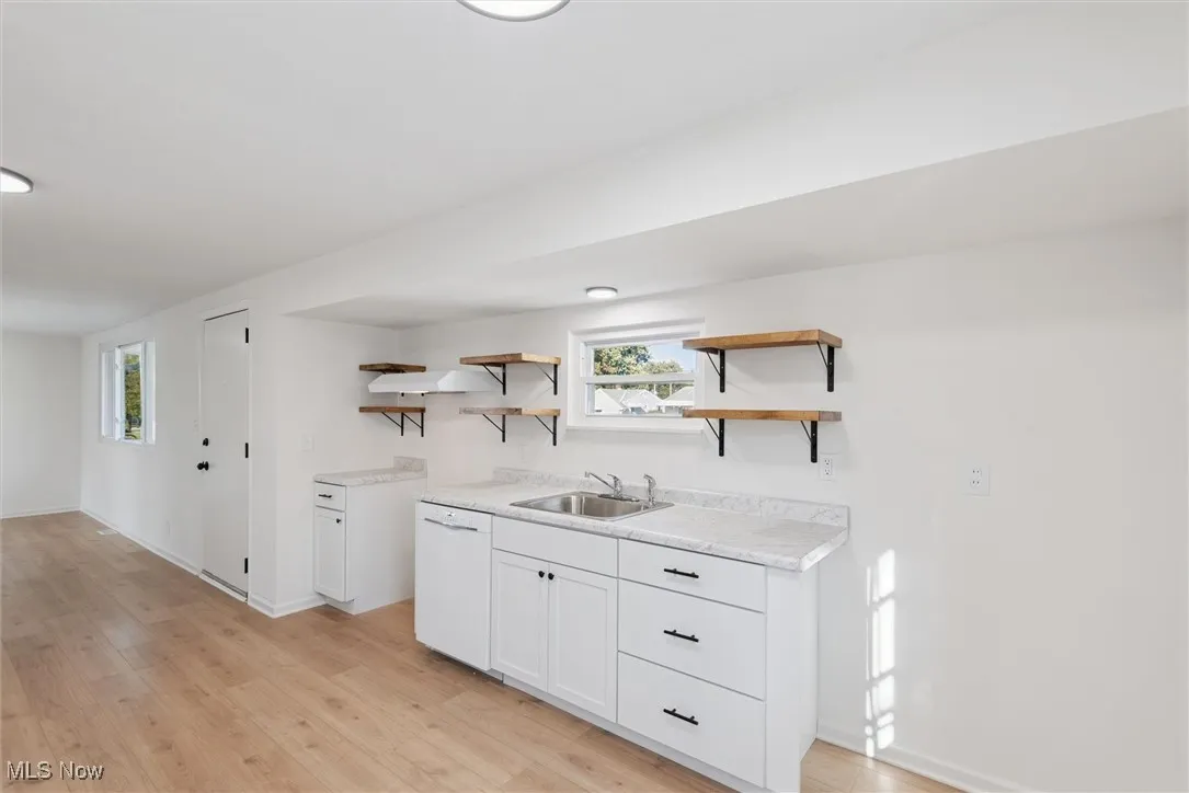 Kitchen with white cabinets, light countertops, open shelves, and dishwasher