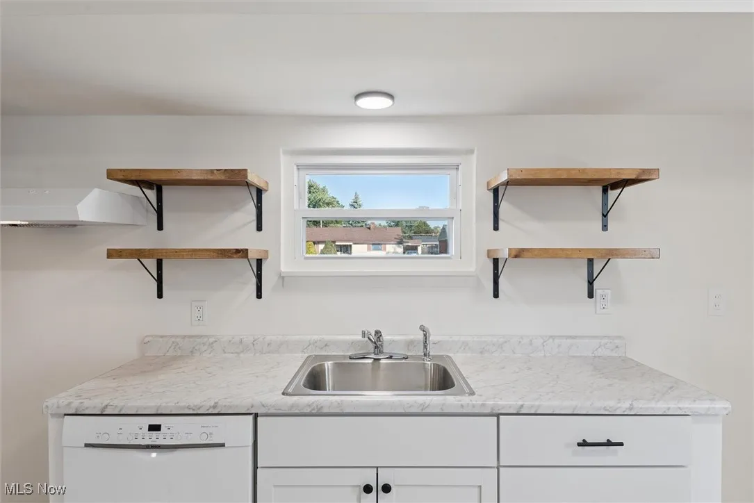 Kitchen with open shelves, white cabinets, white dishwasher, and light countertops