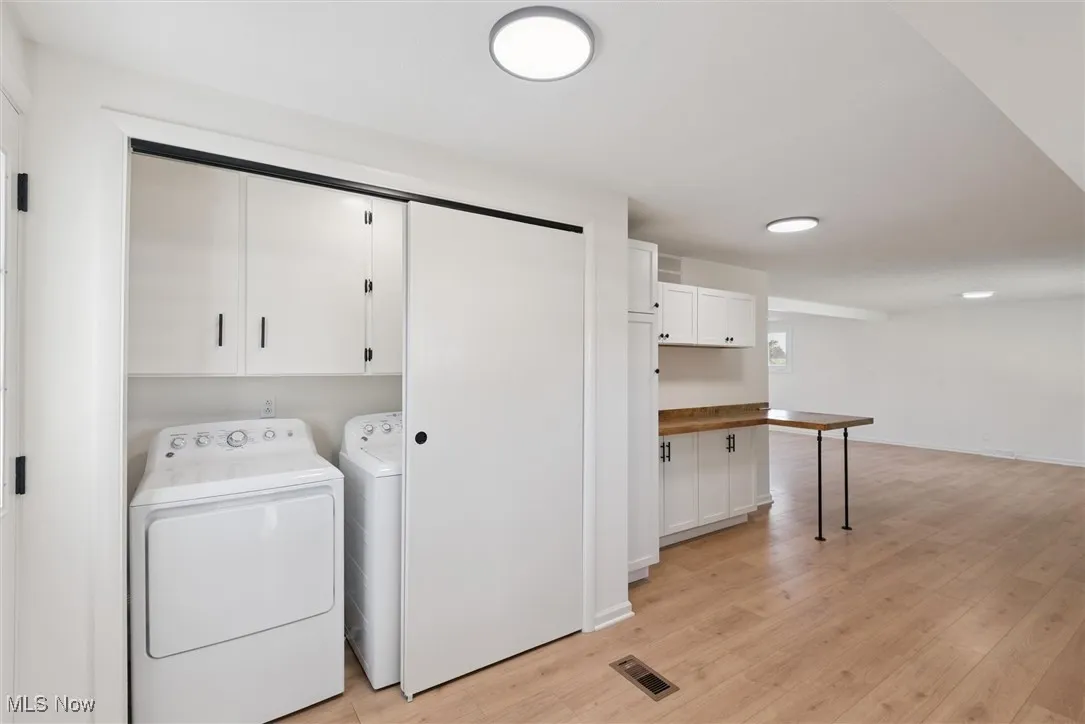 Washroom with cabinet space, washer and clothes dryer, and light wood-type flooring
