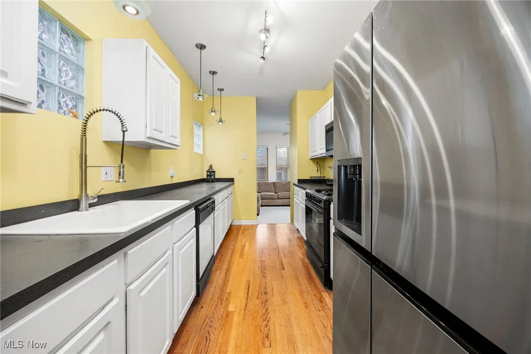 Kitchen with stainless steel appliances, dark countertops, white cabinets, and light wood-style flooring