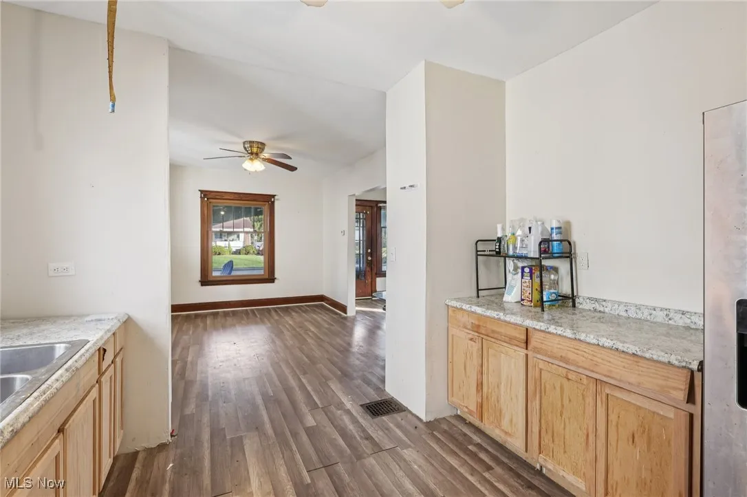 Kitchen featuring light brown cabinets, dark wood finished floors, stainless steel fridge with ice dispenser, a ceiling fan, and light stone counters