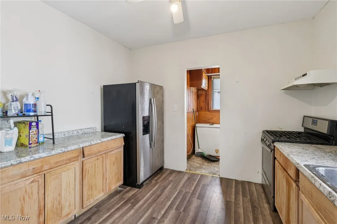 Kitchen with appliances with stainless steel finishes, under cabinet range hood, dark wood-style floors, and light stone counters