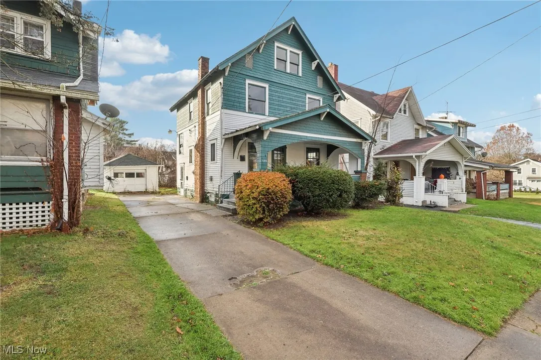 American foursquare style home featuring a porch, a front lawn, driveway, an outdoor structure, and a detached garage