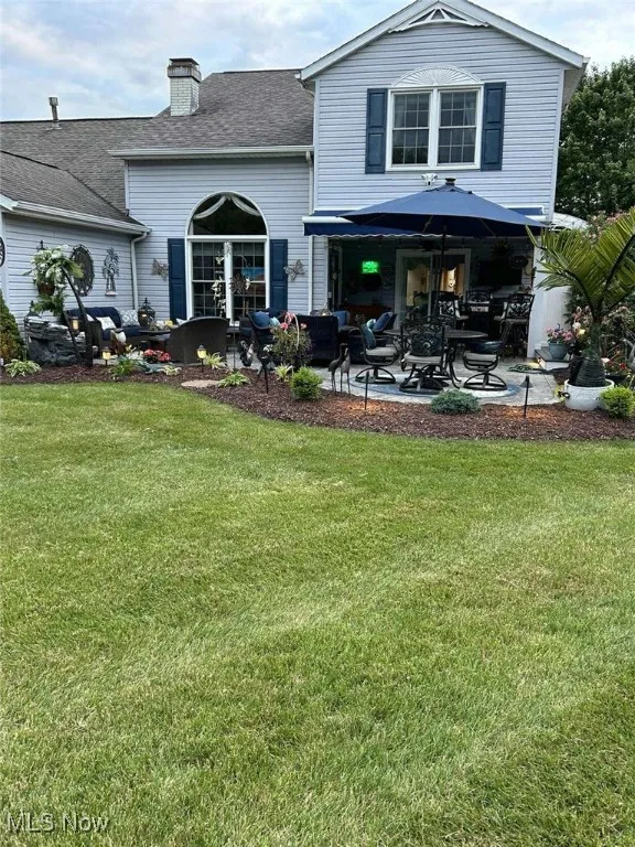Rear view of house featuring a patio, a lawn, a shingled roof, and a chimney