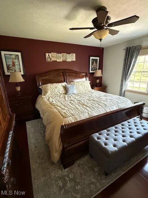 Bedroom featuring a ceiling fan, dark wood-style floors, and a textured ceiling