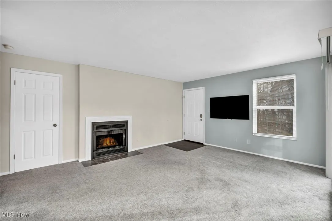 Unfurnished living room with a fireplace with flush hearth and carpet flooring