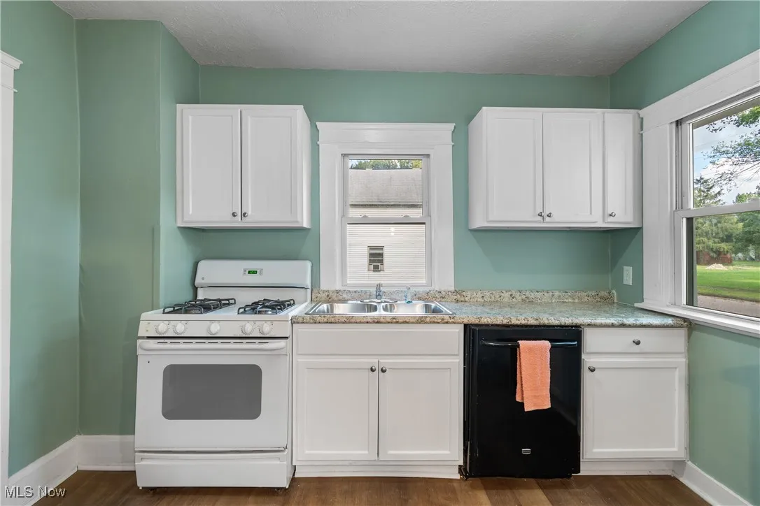 Kitchen with white gas range, white cabinets, dishwasher, and a textured ceiling