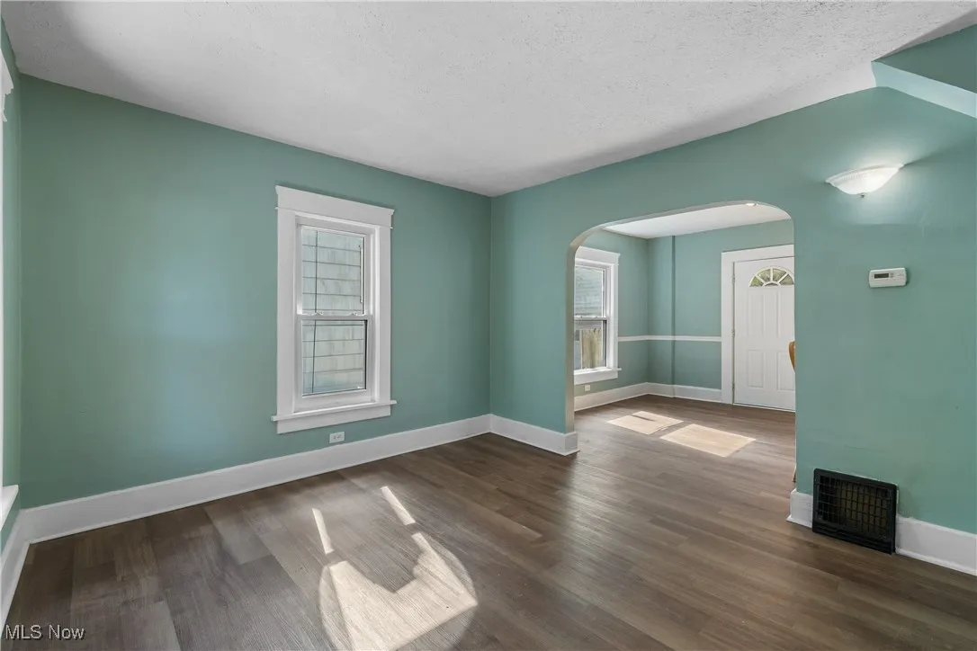 Spare room with healthy amount of natural light, dark wood-type flooring, arched walkways, and a textured ceiling