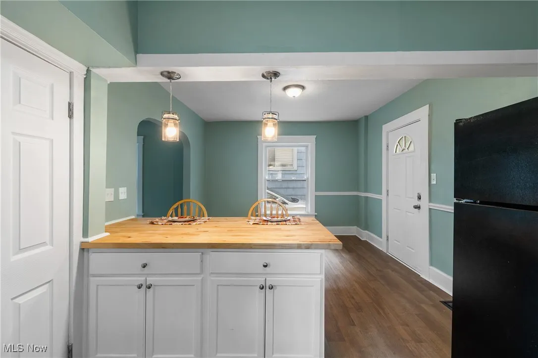 Kitchen featuring freestanding refrigerator, pendant lighting, a peninsula, butcher block counters, and dark wood-style floors