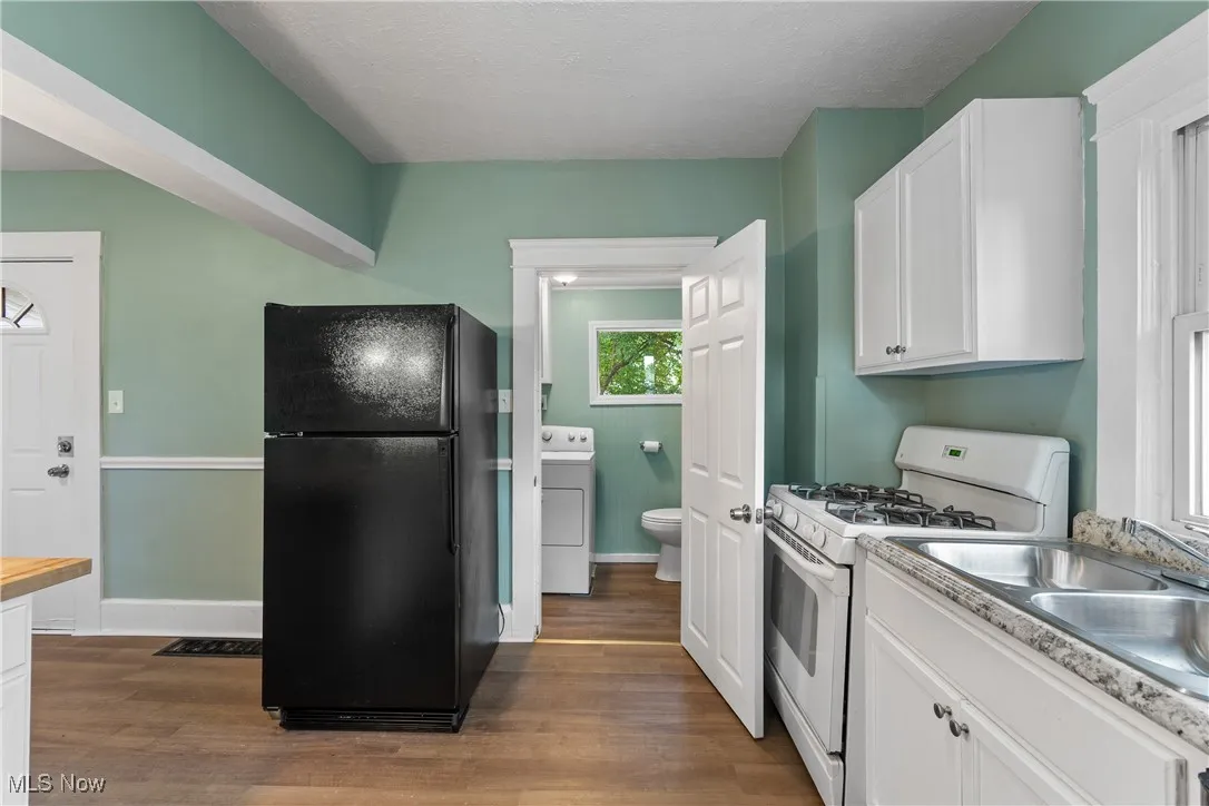Kitchen with white range with gas stovetop, freestanding refrigerator, white cabinets, dark wood-type flooring, and a textured ceiling