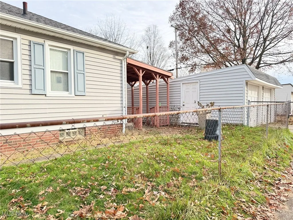 View of property exterior featuring an outdoor structure, a patio, roof with shingles, and a detached garage