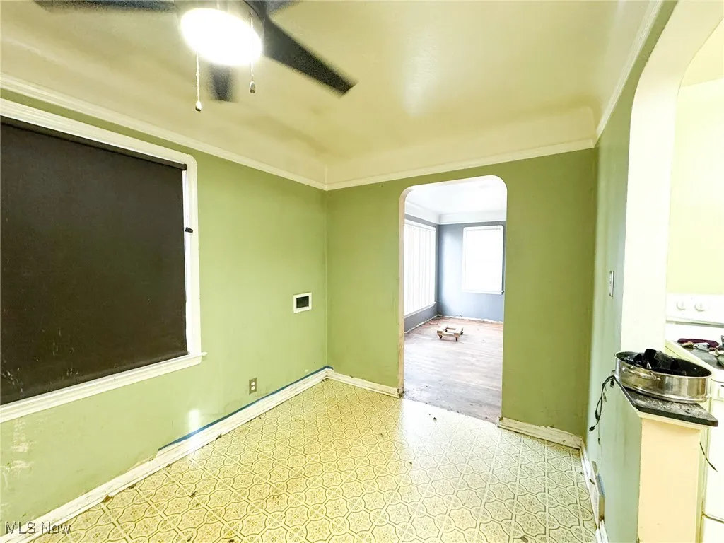 Empty room with light flooring, arched walkways, crown molding, and ceiling fan