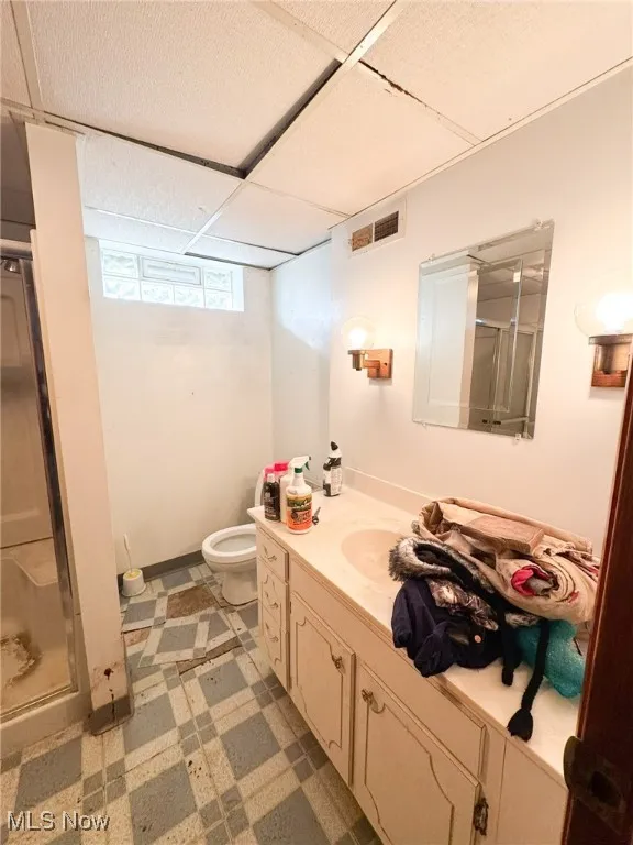 Full bathroom in basement featuring a stall shower, light flooring, vanity, and a paneled ceiling