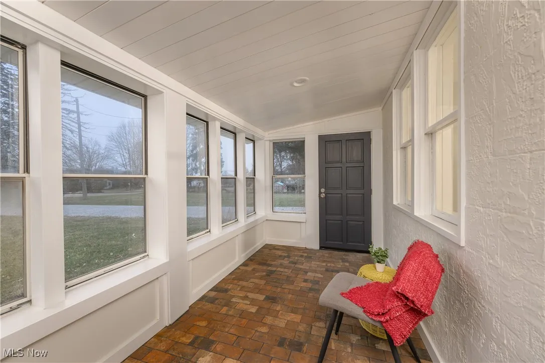 Sunroom featuring brick floors, lofted ceiling, and a textured wall