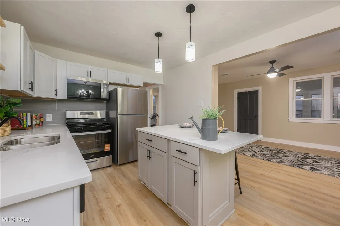 Kitchen with a breakfast bar, stainless steel appliances, white cabinets, hanging light fixtures, and decorative backsplash