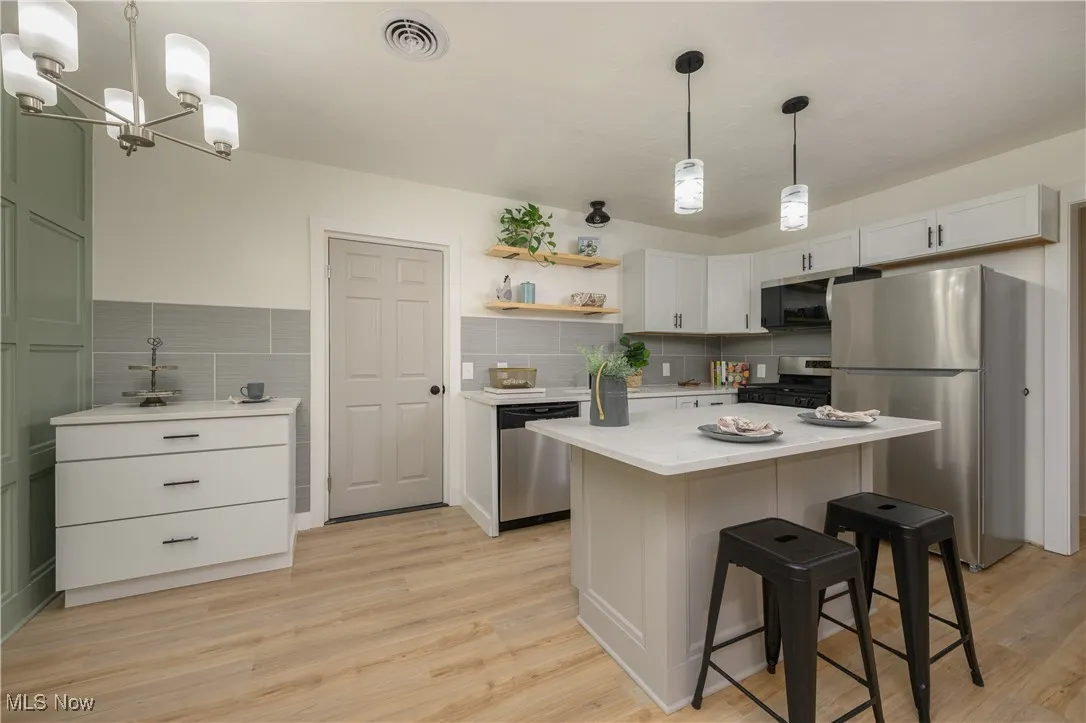 Kitchen with appliances with stainless steel finishes, decorative light fixtures, open shelves, and light wood-style floors
